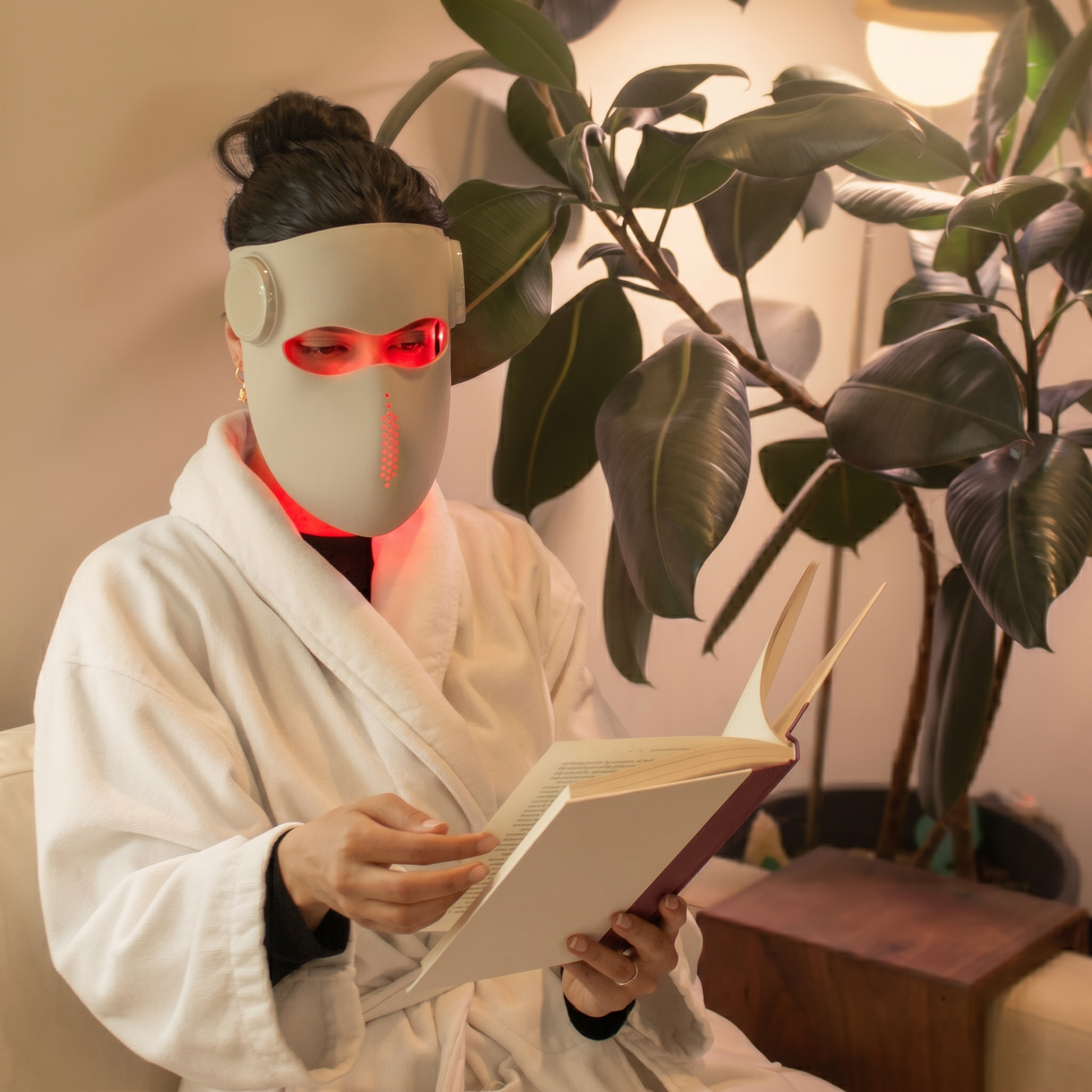 Woman in white robe reading with Renuveil LED mask on